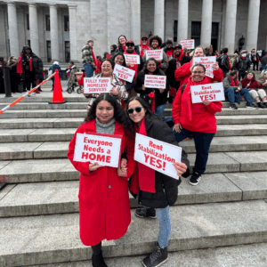 Housing and Homelessness Advocacy Day advocates from across the state of Washington gathered at the capitol steps in Olypia wearing iconic red scarves, as red is the color of homelessness and housing advocacy. Signs they hold read, "Everyone needs a home" and "Rent Stabilization Yes!)